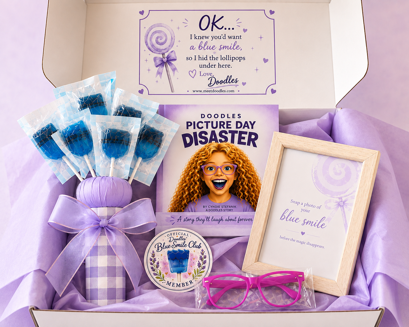 The Blue Smile Experience Gift Box — open box showing book, lollipops, glasses and keepsake frame